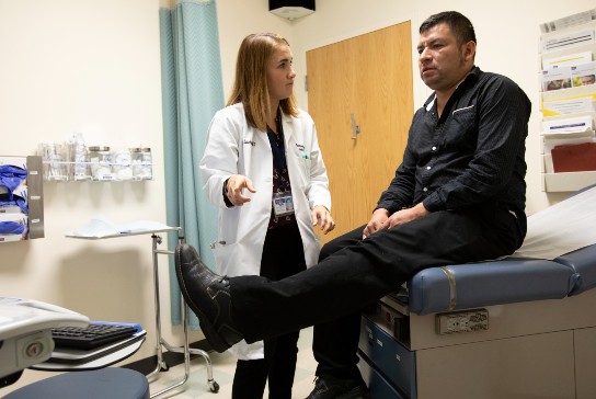 Doctor points to patient's outstretched leg as they converse in an exam room.